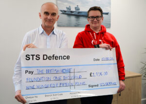 A male representative from the British Heart Foundation receives a prop donation cheque from STS Defence with the amount reading as £1,915