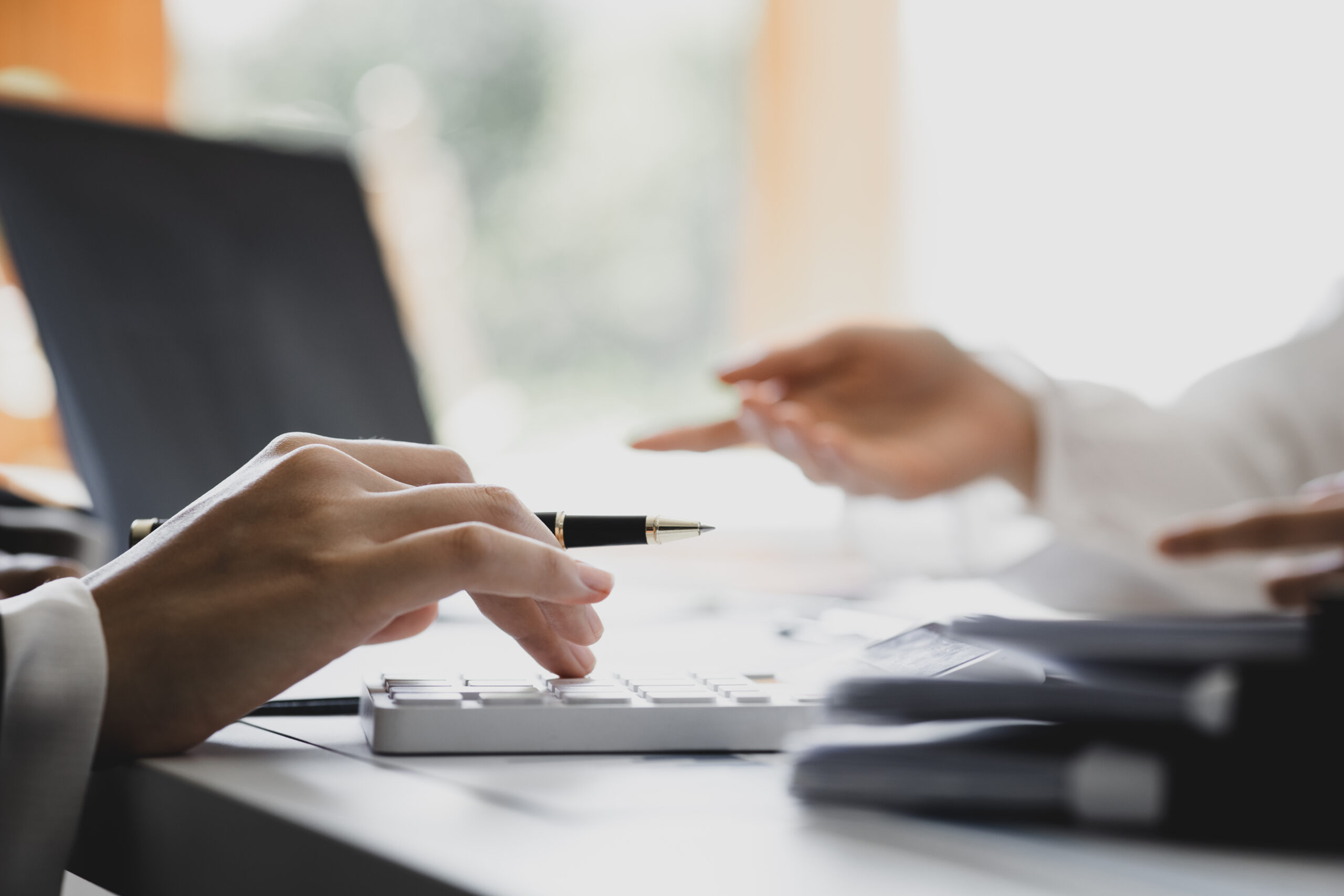 A stock image of two people having a meeting. One is holding a pen and there is a laptop in the background.