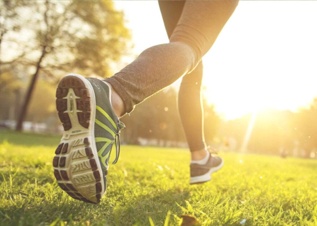 A stock image of a runner going for a run on grass. It is a close-up action shot of their trainer clad feet.