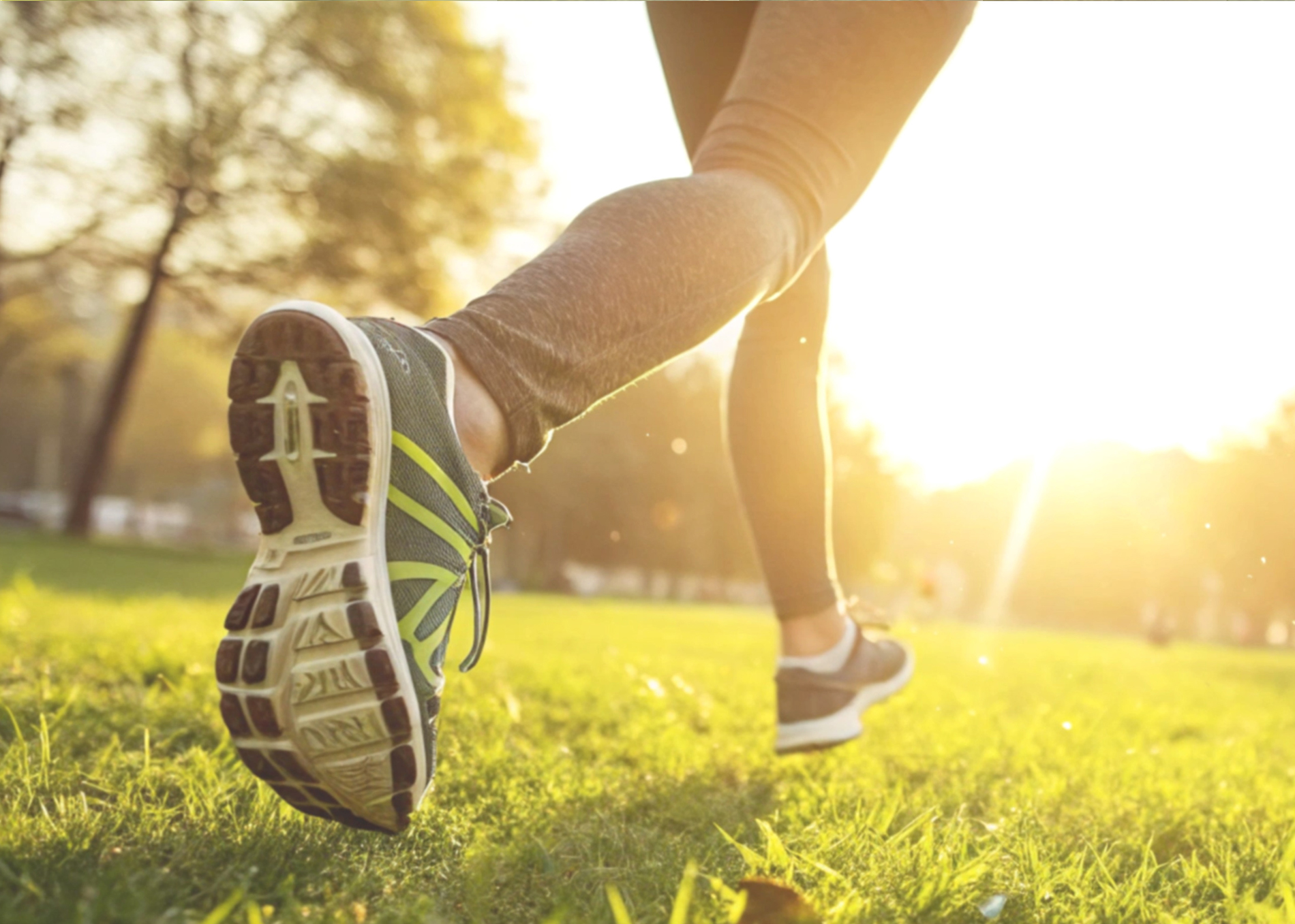 A stock image of a runner going for a run on grass. It is a close-up action shot of their trainer clad feet.