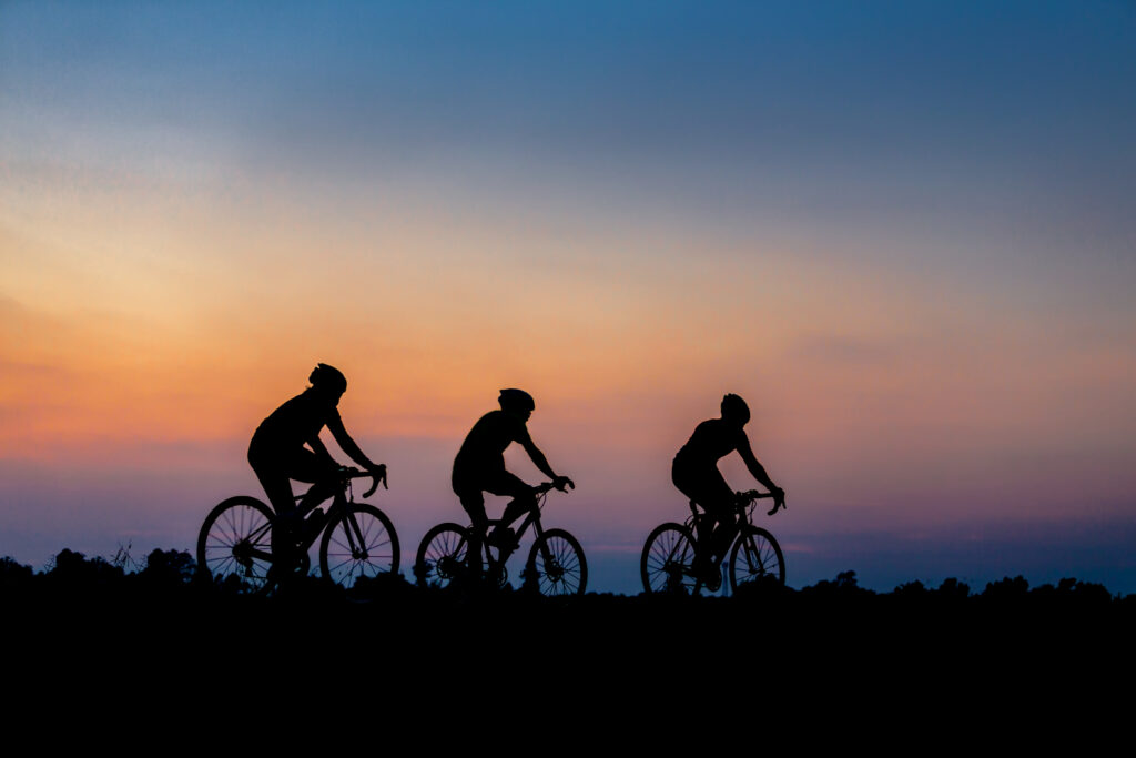 A stock image of a silhouette of three cyclists riding against a beautiful sunset