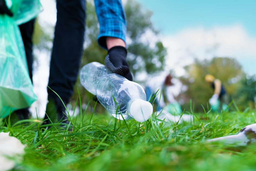 A stock image of a man picking up bottle into rubbish bags while doing a park clean.
