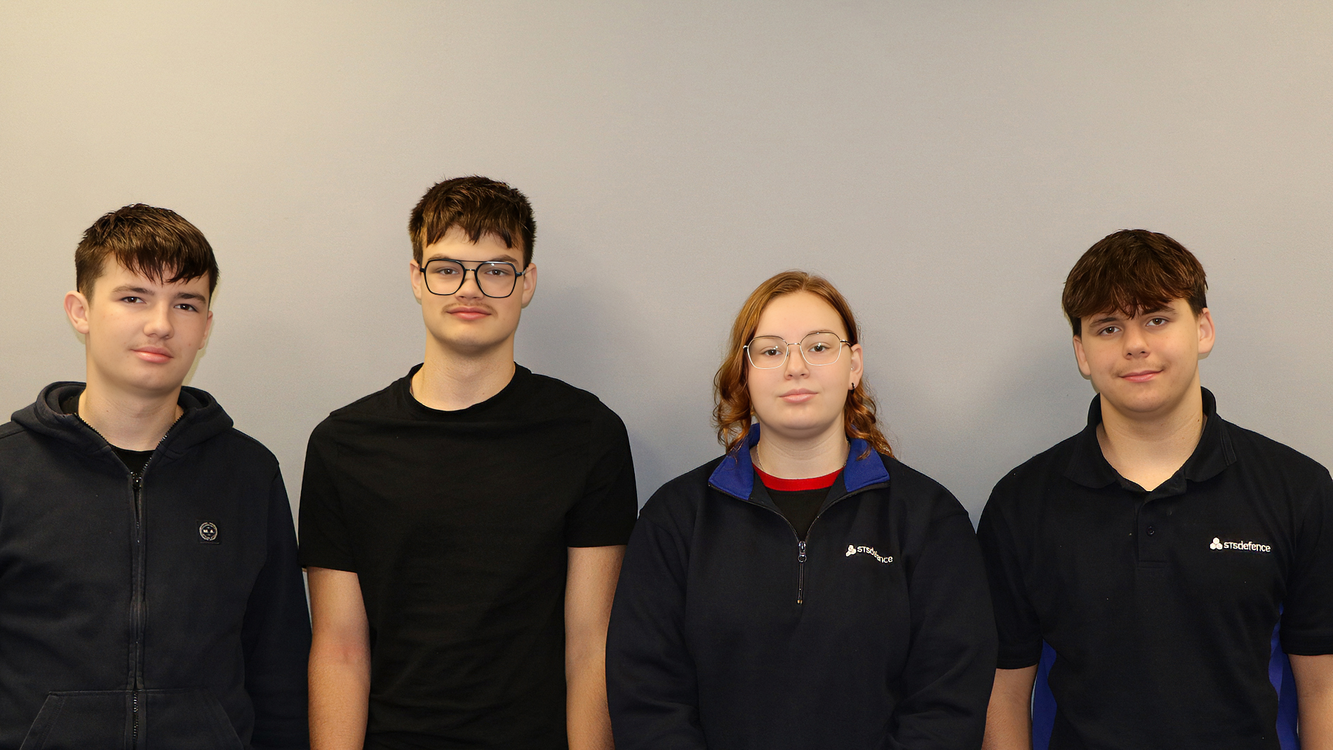 A group of four STS Defence apprentices stood against a grey wall facing the camera